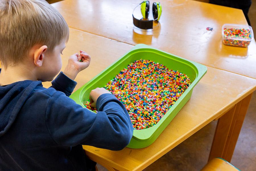 A child sits at a table playing with Perler beads. 