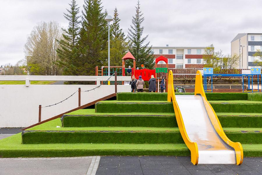 Steps with artificial grass and a slide. Playground equipment in the background. 