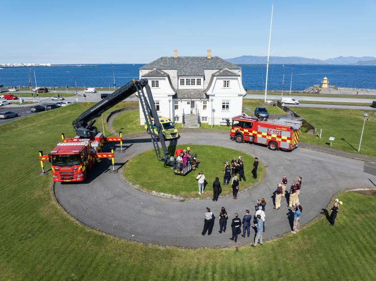 Slökkviliðsbílar og sjúkrabíll uppstilltir við Höfða í blíðviðri þegar tekið var á móti brunabangsanum Björnis. Loftmynd.