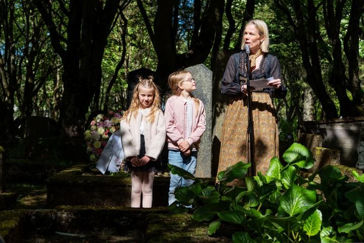 At Hólavallagarður, Björg Magnúsdóttir, president of City Council, delivers remarks. Jóný and Nína look on.