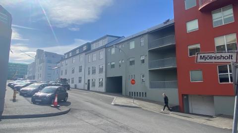 Auð gata og hús. Nokkrum bílum lagt við götuna.