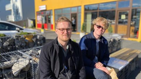 Two men sit on a bench outside Brauð &amp; Co at Laugalækur.