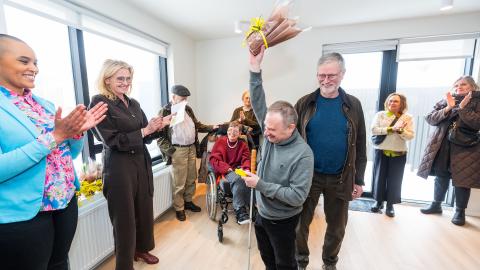 Kjartan Ásmundsson raises a bouquet of flowers like a trophy to celebrate receiving keys to his new home. The mayor and the chair of the Welfare Council also appear in the photo. 